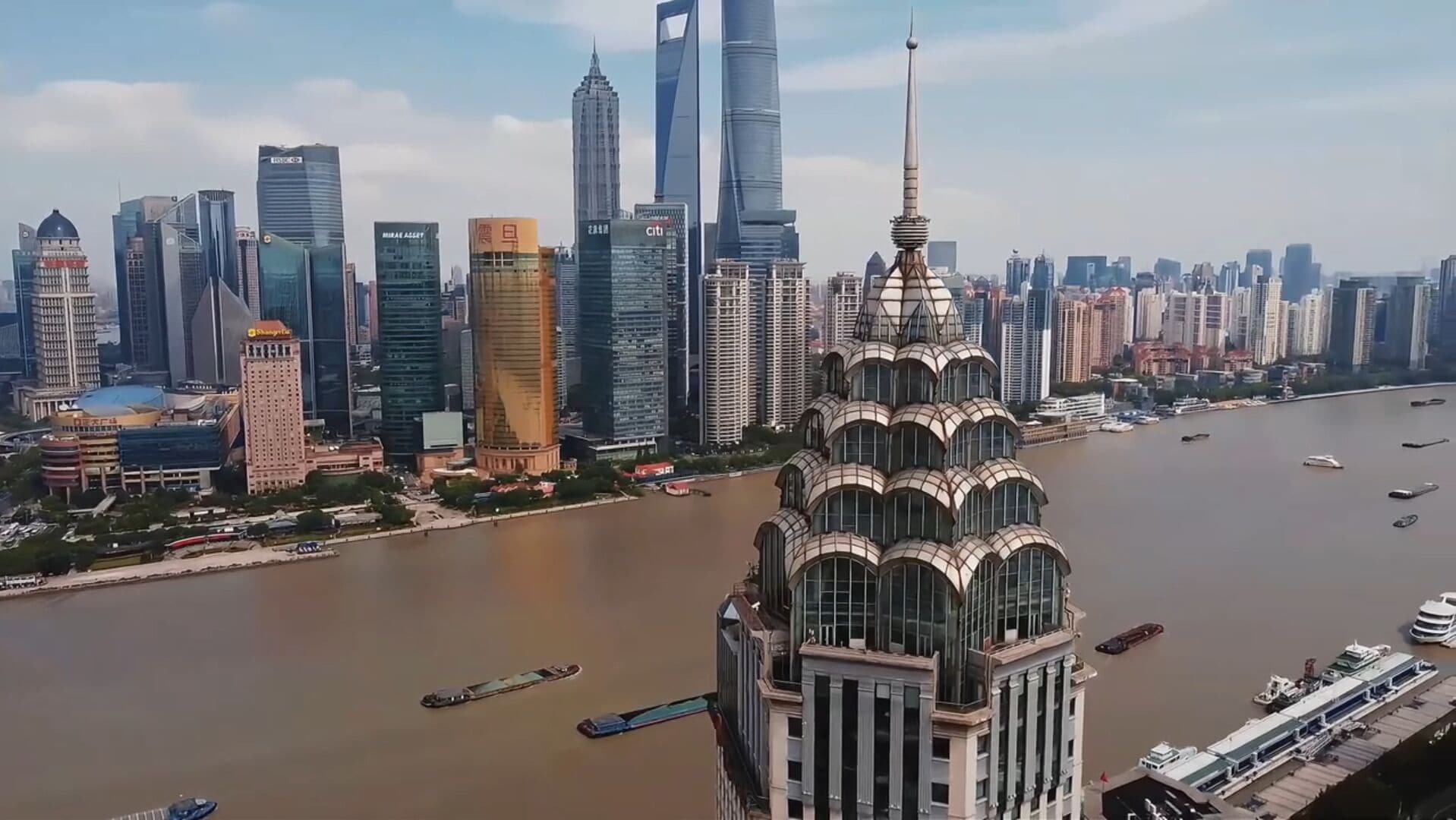 Un paisaje urbano con un edificio destacado, una torre distintiva y un río con barcos.