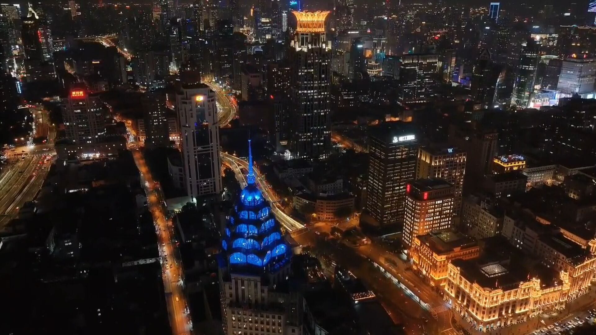 A cityscape at night with illuminated buildings, a prominent blue-lit structure, and a busy road.