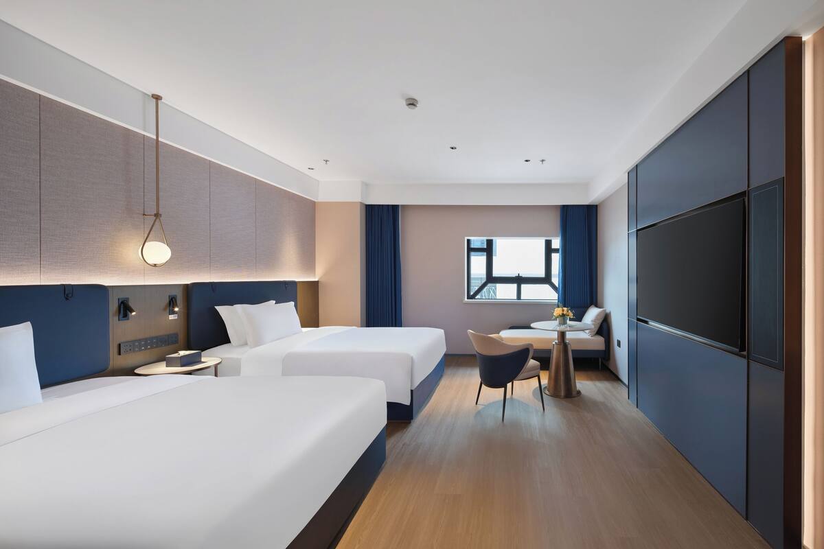 Habitación de hotel con dos camas, un escritorio, una silla, un televisor y una ventana con vistas.