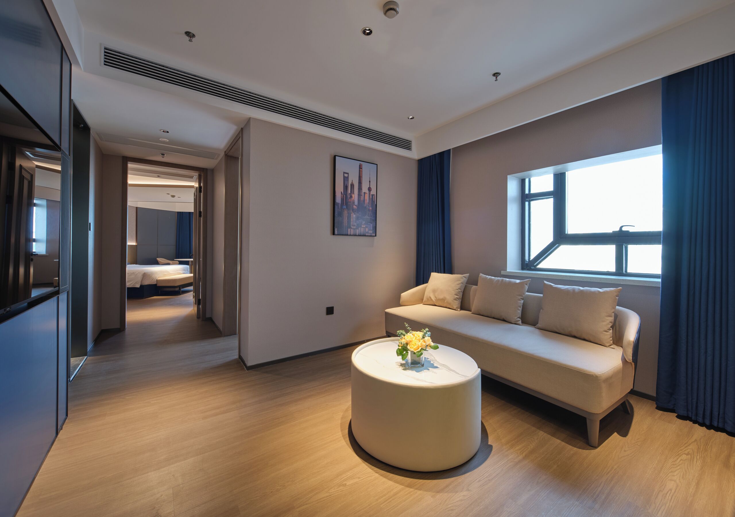 Una habitación de hotel moderna con un sofá, una mesita redonda y un cuadro de paisaje urbano en la pared.