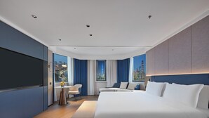 Ein modernes Hotelzimmer mit einem großen Bett, einer Sitzecke mit kleinem Tisch und Blick auf die Stadt durch große Fenster.