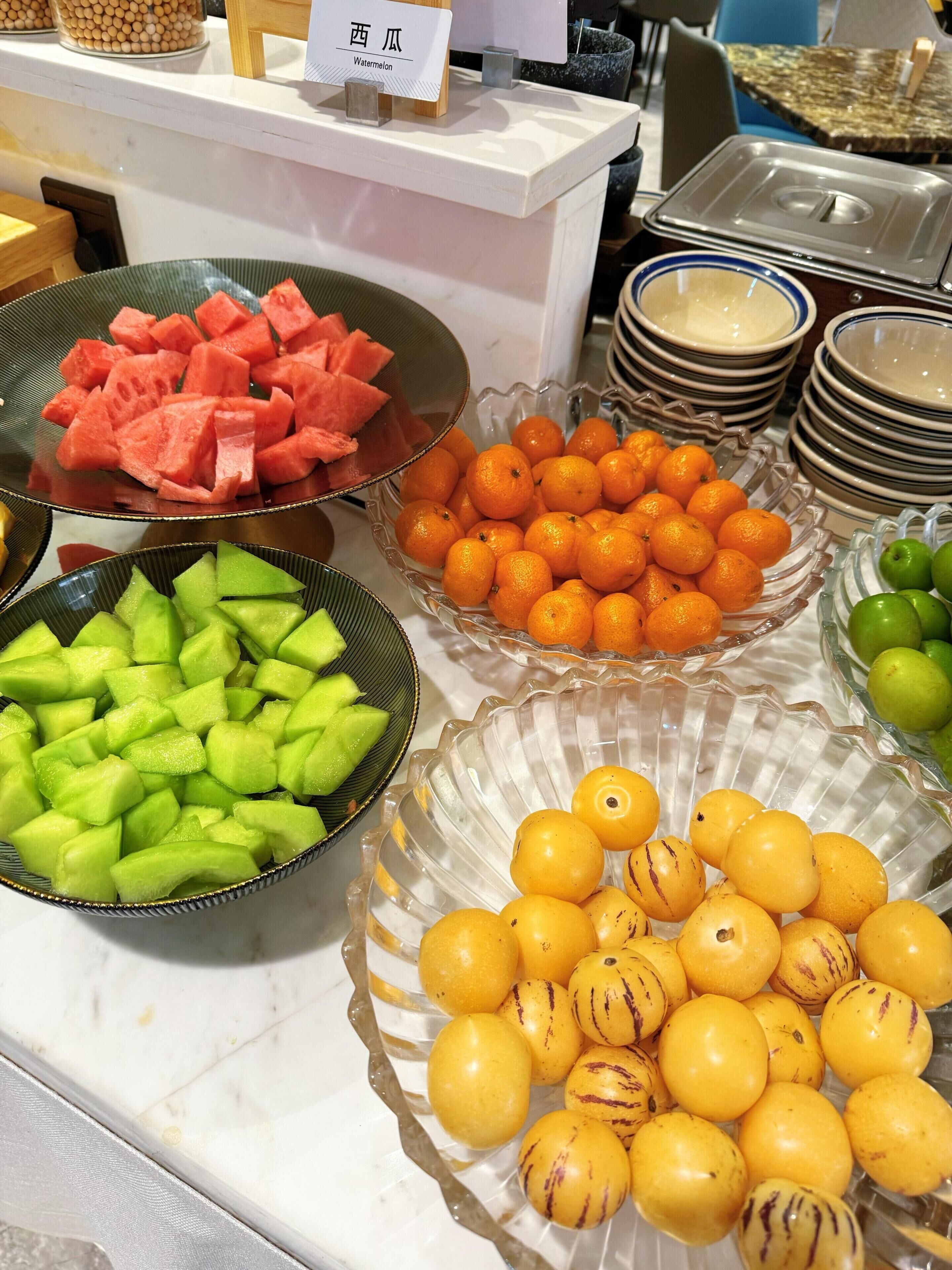 A buffet table with various fruits including watermelon, oranges, and cantaloupe.