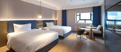 A modern hotel room with two beds, a small seating area, and a large window.