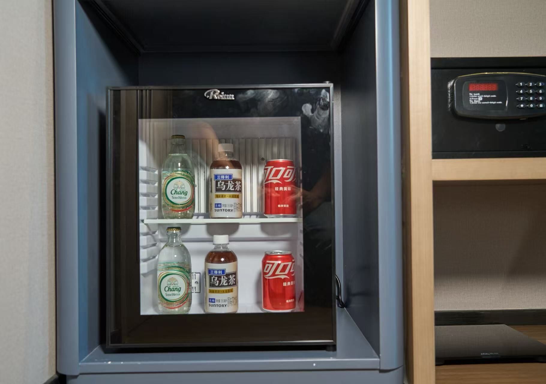 Un minibar con una bottiglia di Chang Soja Water, una bottiglia di whisky Suntory e due lattine di Coca-Cola.