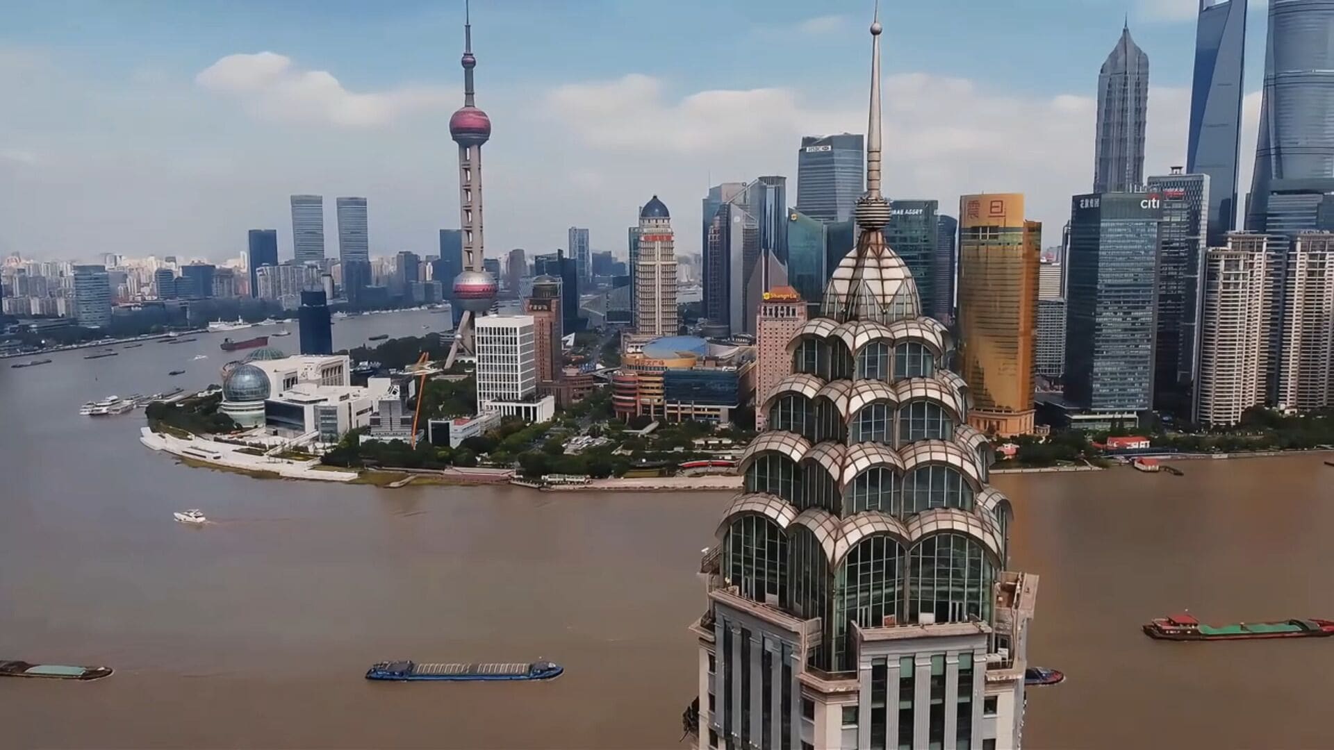 A cityscape with modern skyscrapers, a prominent tower with a spherical observation deck, and a river with boats.