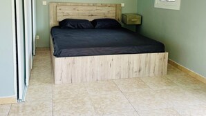 Une chambre à coucher avec un cadre de lit en bois, un matelas noir, une table de chevet et une fenêtre donnant sur un paysage verdoyant.
