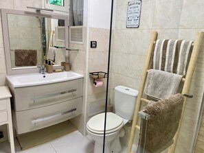 Een badkamer met een wit wastafelmeubel, spiegel en toilet. Er is een handdoekhouder met een gestreepte handdoek en een zachte handdoek. Een bord op de muur geeft de regels voor de badkamer weer.