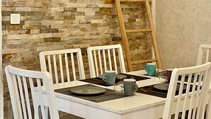 Un coin repas avec un mur en pierre, des chaises blanches et une échelle en bois appuyée contre le mur.