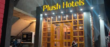 A building with a sign reading "Plush Hotels" and a red scooter parked in front.