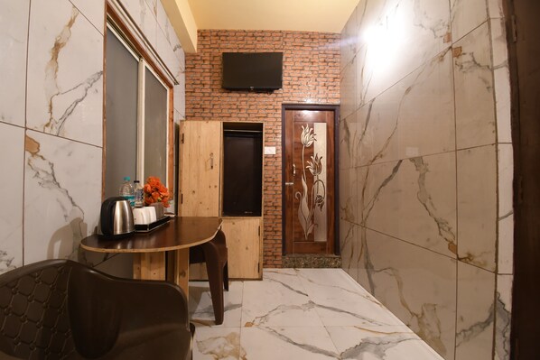 A small, compact room with a wooden table, a chair, a television mounted on the wall, and a door with a decorative panel. - Hotel Plush (Puri)