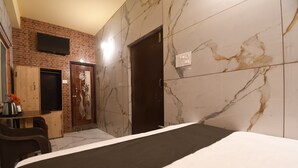 Ein Hotelzimmer mit einem Bett, einem Holztisch, einem an der Ziegelwand befestigten Fernseher und einer Tür.