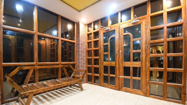 Ein Zimmer mit großen Fenstern mit Holzrahmen, einer hölzernen Bank und einem Fliesenboden.