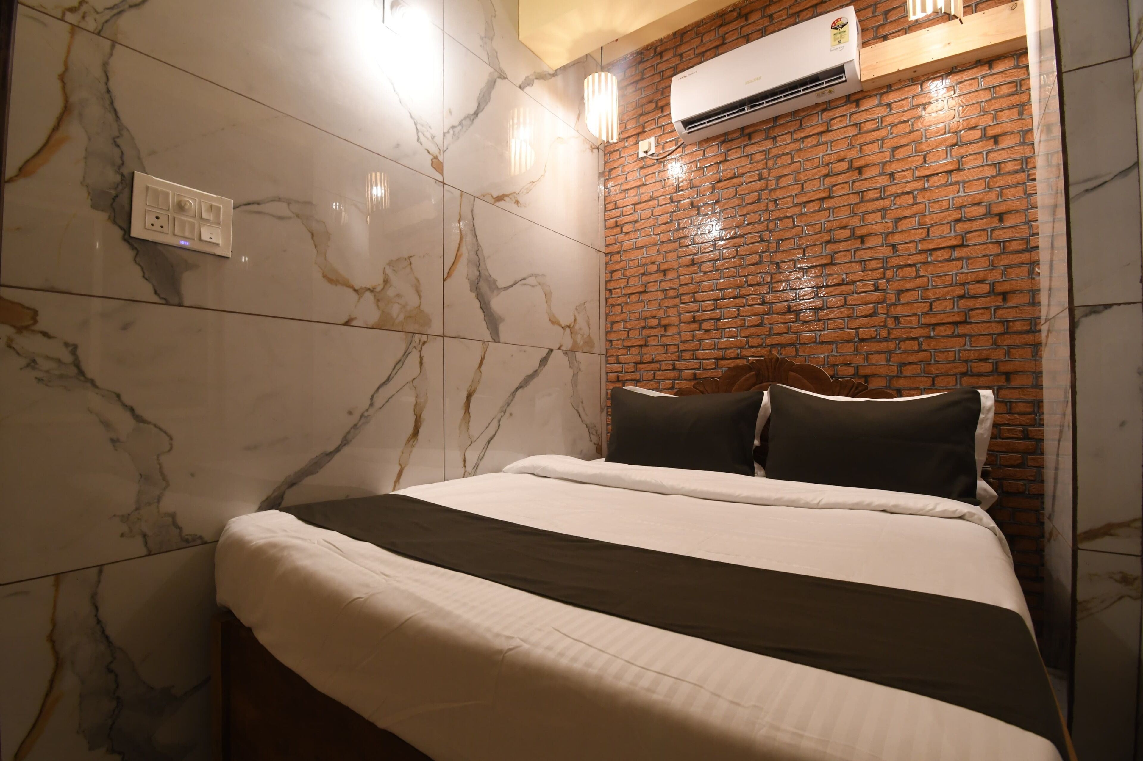 Una habitación de hotel con cama, paredes de mármol, un muro decorativo de ladrillo y un equipo de aire acondicionado.
