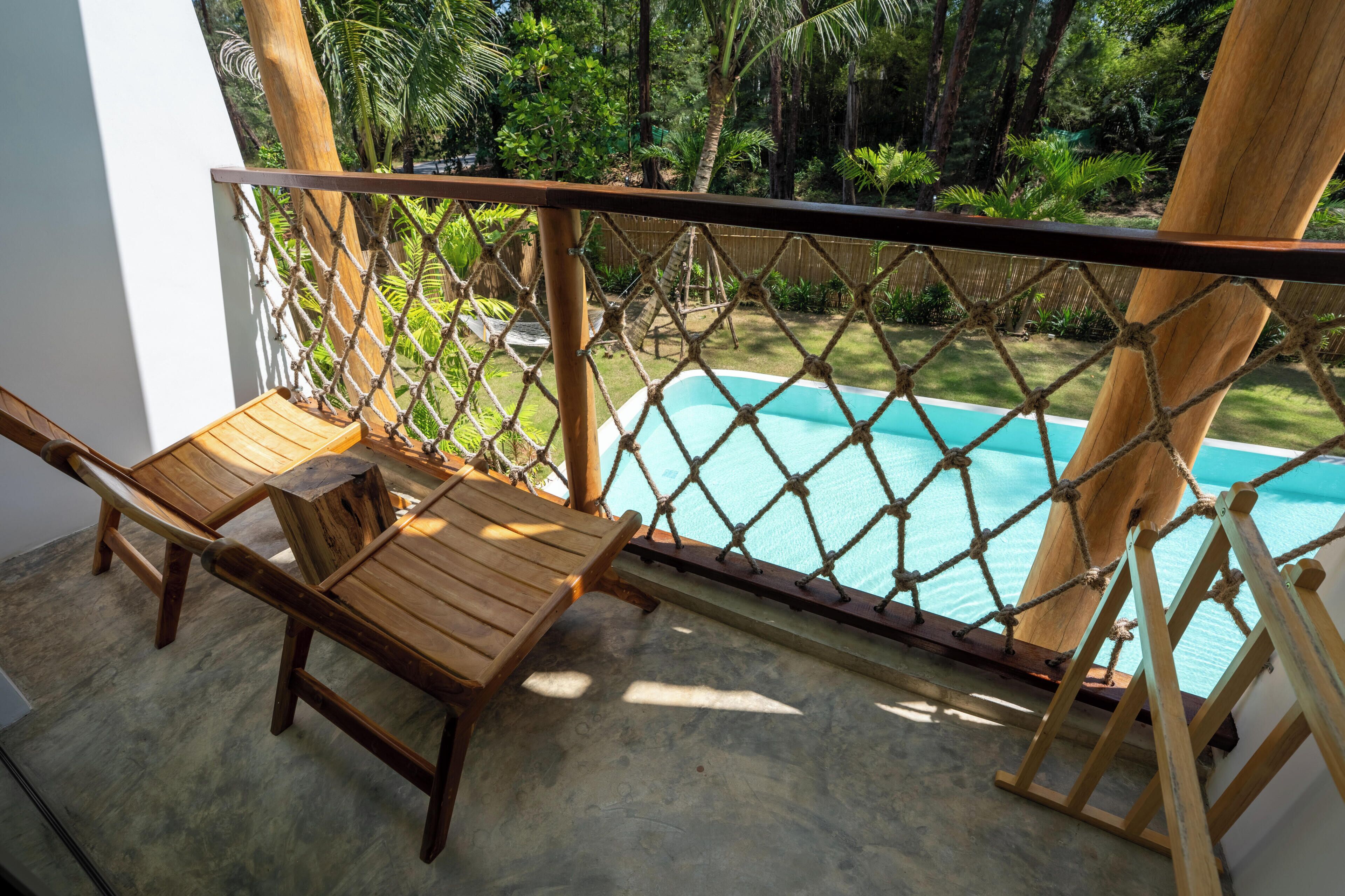 A wooden deck with a rope barrier, a pool, and lush greenery.