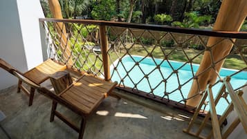 Una terraza de madera con una barandilla de cuerda, una piscina y abundante follaje.