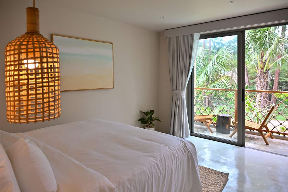 Ein Schlafzimmer mit einem großen Bett, einer Hängelampe, einem gerahmten Bild und Blick auf einen Balkon mit Gartenmöbeln.