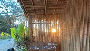 Eine Bambuskonstruktion mit einem Schild, auf dem 'THE TALAY' steht, und einem Kiesweg, der dorthin führt.