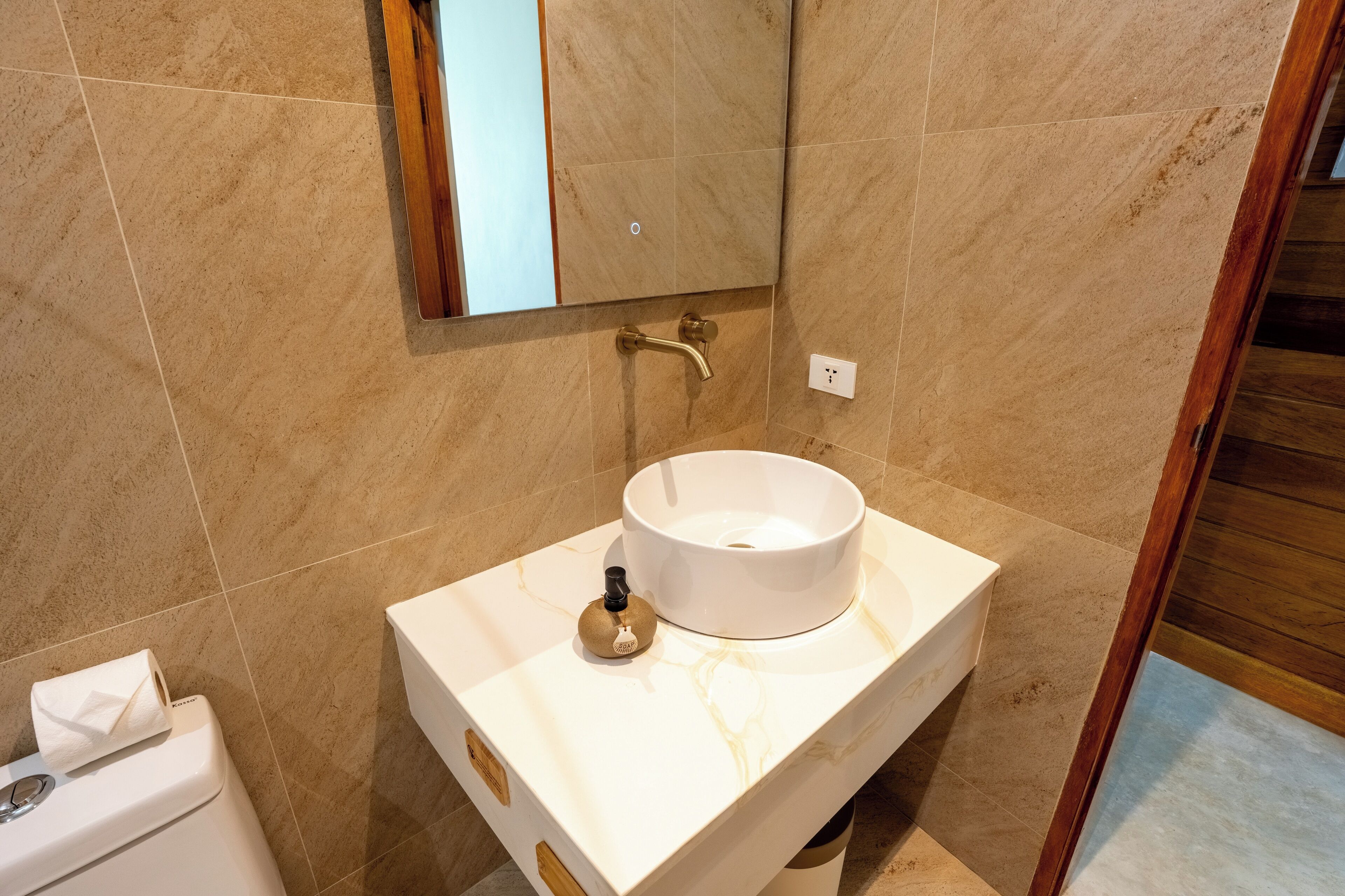 A bathroom with a marble sink, a mirror, and a towel dispenser.