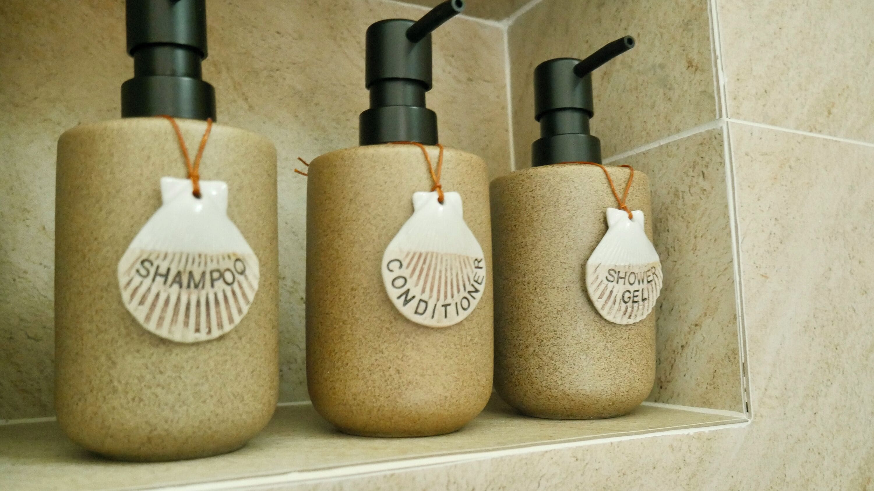 Three bathroom bottles with labels for shampoo, conditioner, and shower gel.