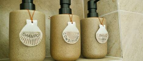 Three bathroom bottles with labels for shampoo, conditioner, and shower gel.