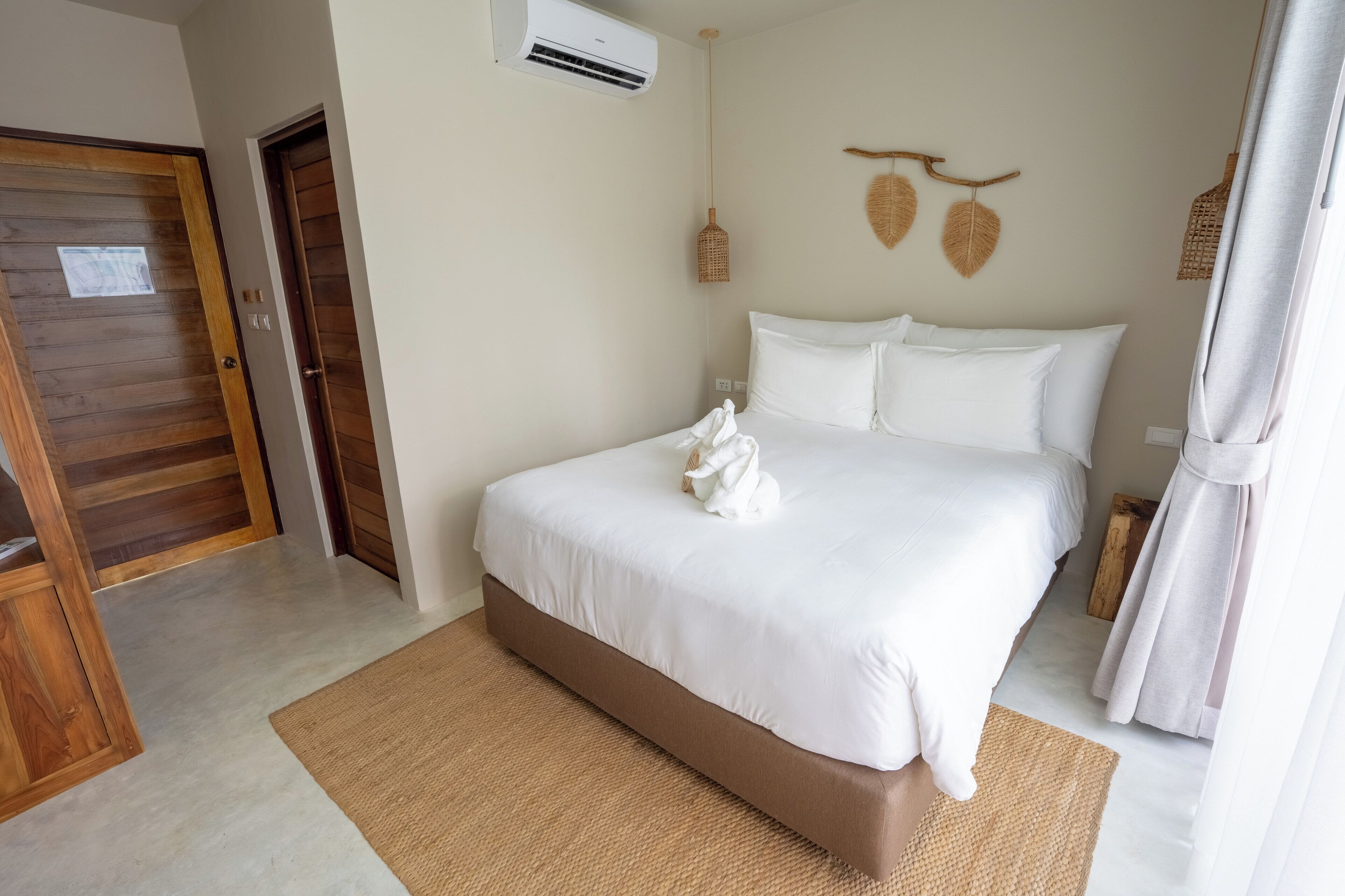 A bedroom with a bed, a wooden door, an air conditioning unit, and a woven wall hanging.