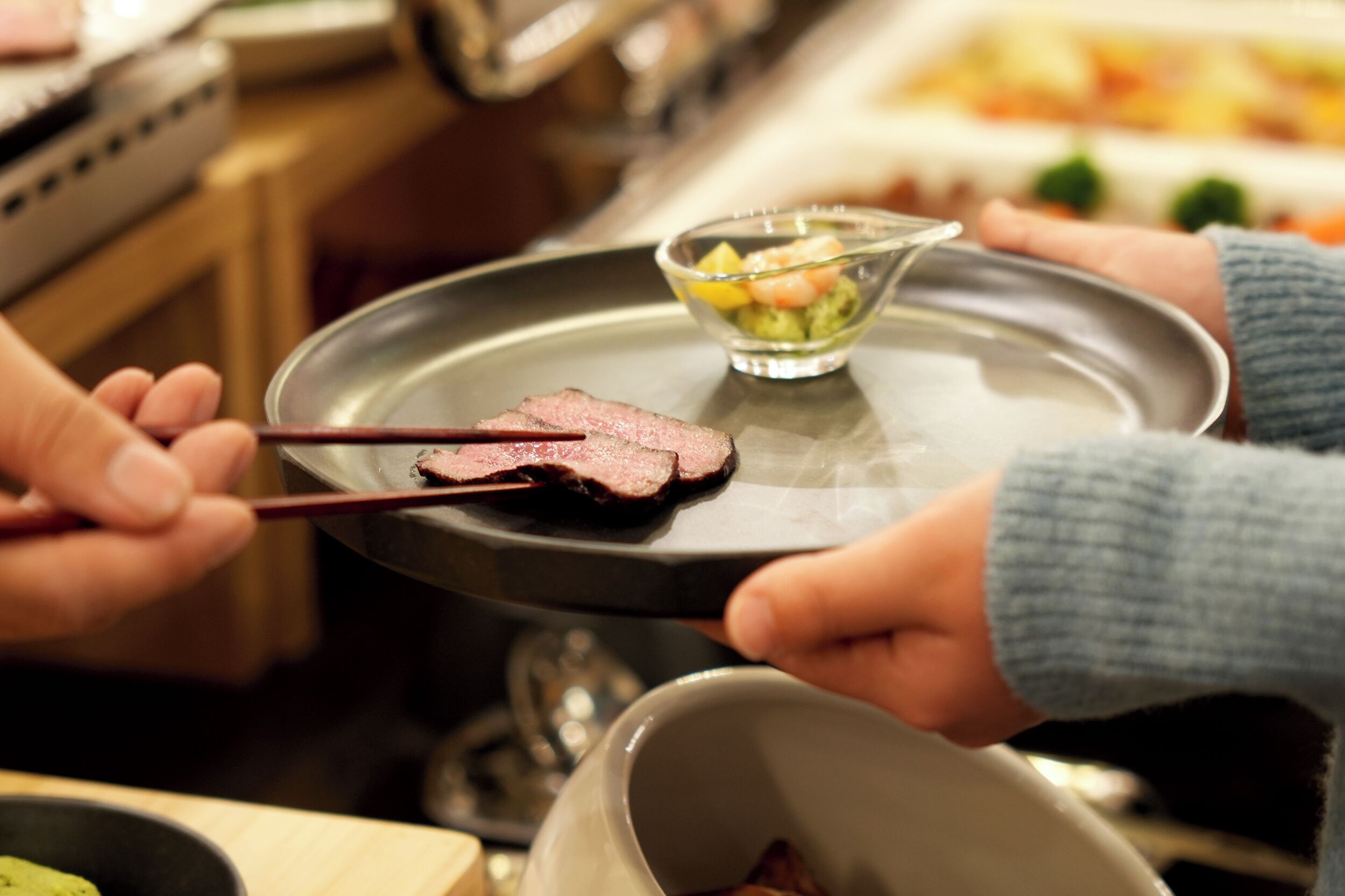 A person holding a tray with a piece of meat and a small bowl of salad.