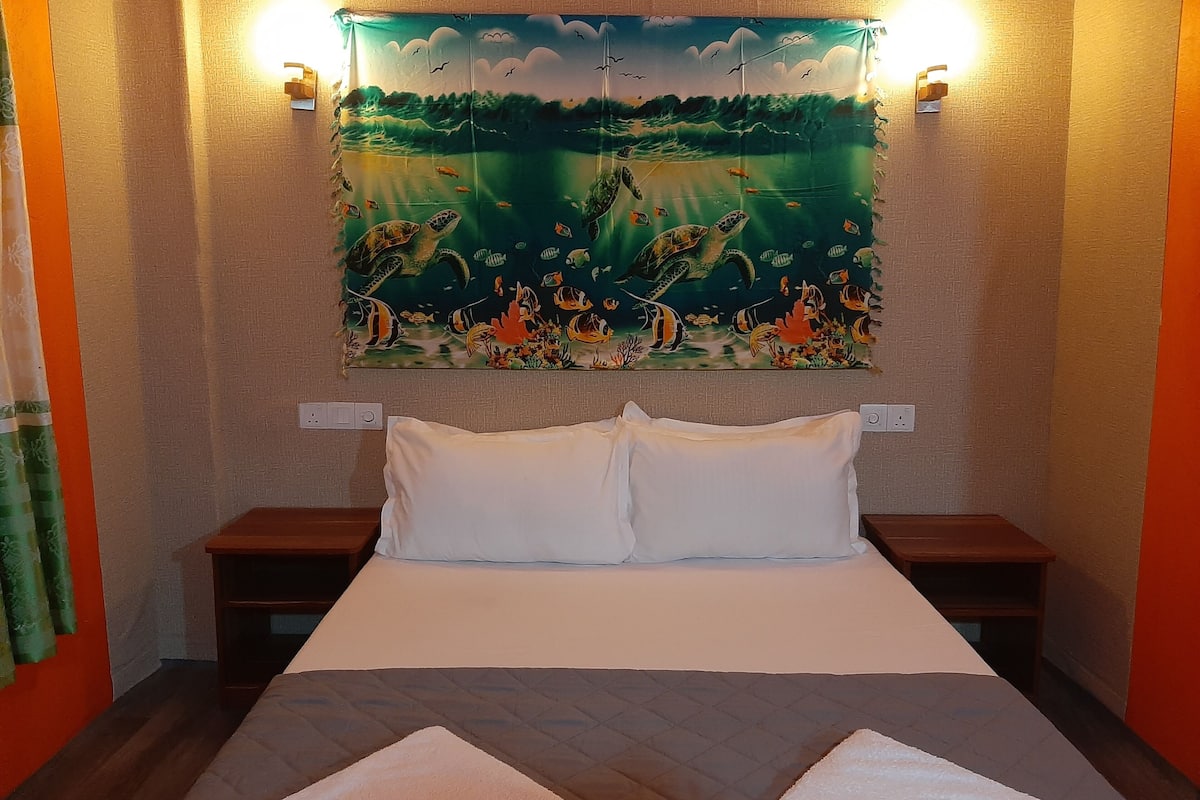 Une chambre d’hôtel avec un grand lit, deux tables de chevet et une tapisserie représentant la vie marine, accrochée au mur.