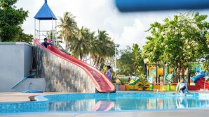 A swimming pool with a red slide, palm trees, and a colorful play structure. - SEASUNBEACH MAAFUSHI (Maafushi)