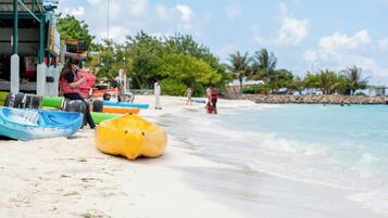 Una playa con botes inflables, un edificio con techo verde y palmeras al fondo.