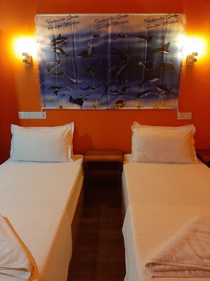 Une chambre d’hôtel avec deux lits simples, du linge de lit blanc, une œuvre d’art fixée au mur représentant la vie marine, et une petite table de chevet en bois.