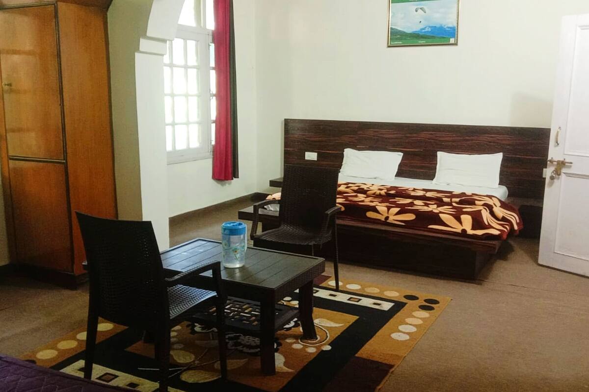 A hotel room with a bed, a desk with a chair, a wardrobe, and a window with curtains.