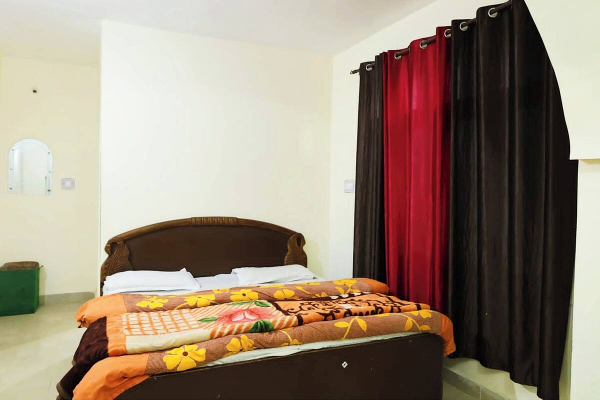A bed with a floral bedspread, a wooden headboard, and a red and black curtain.