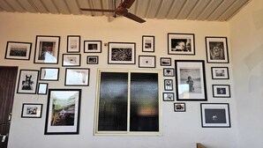 A room with a ceiling fan, a large window with a textured glass door, and multiple framed pictures on the walls. - Aaroha Hill Top (Gokarna)