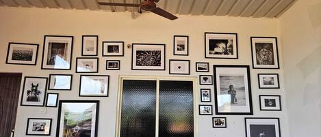 Una habitación con ventilador de techo, un ventanal con puerta de vidrio texturizado y varias fotografías enmarcadas en las paredes.
