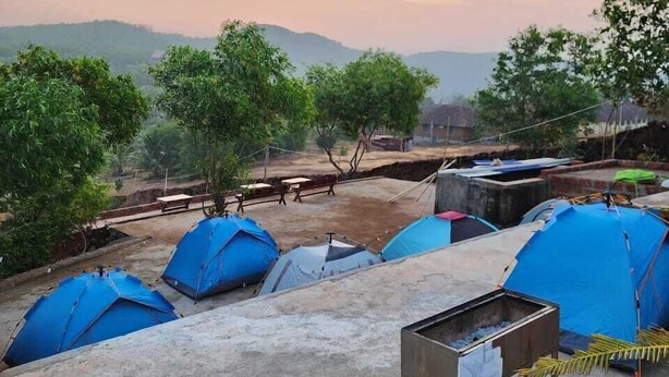 A campsite with multiple blue tents, a metal grill, and a view of distant hills. - Aaroha Hill Top (Gokarna)