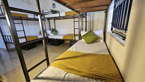 A dormitory room with bunk beds, a window with bars, and a small picture on the wall. - Aaroha Hill Top (Gokarna)