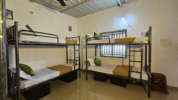Two bunk beds with metal frames, each with a mattress and pillows. There is a window with bars on one bed, and a small stool is visible on the floor.