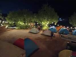 Un campamento por la noche con varias tiendas de campaña y luces colgantes.