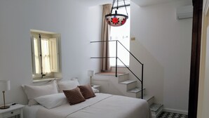 A bedroom with a bed, a nightstand, a lamp, a window with curtains, a staircase, and a checkered floor. - Rooftop mansion (Palermo)