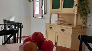 A dining table with a fruit bowl containing apples, a wooden cabinet with a green door, and a window with a pink frame. - Rooftop mansion (Palermo)