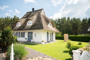 Ein Haus mit einem Strohdach, heller Fassade, blauer Tür und einem gepflegten Rasen.