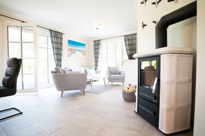 A modern living room with a fireplace, a sofa, a chair, and a dining table. - Vacation home Haubenlerche 15 - Holiday home Haubenlerche 15 - Close to nature (Fuhlendorf)