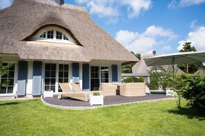 Een rieten huis met een overdekte zithoek en een gazon.