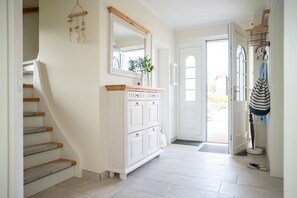 Een trap met houten treden, een wit kastje met lades, een spiegel en een deur naar buiten.