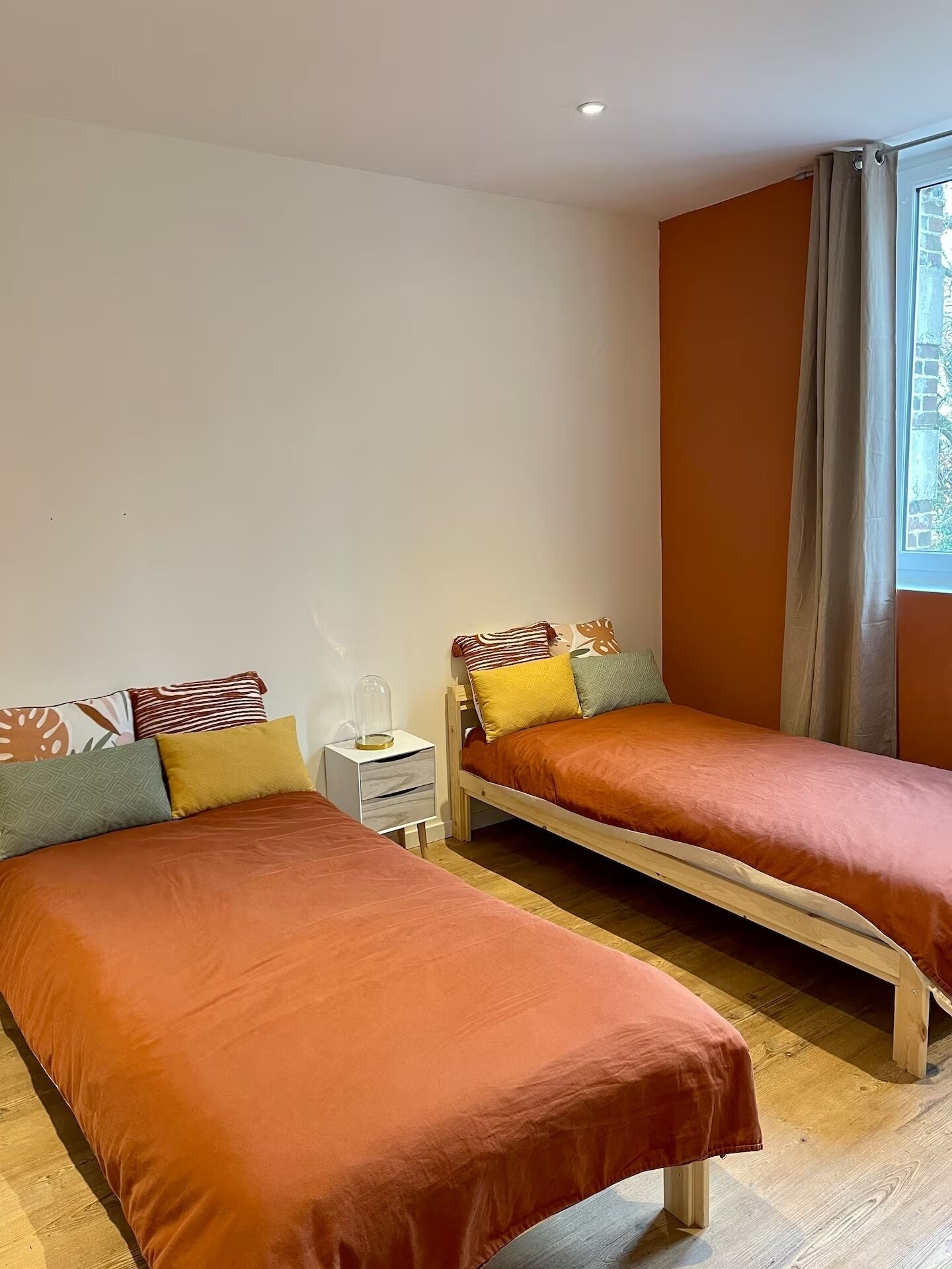 A twin bedroom with two single beds, a nightstand with a lamp, and a window with curtains.