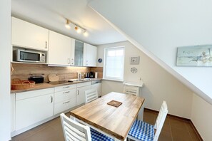 Cocina compacta con armarios blancos, un microondas y una mesa de madera con sillas de tapiz azul a cuadros.