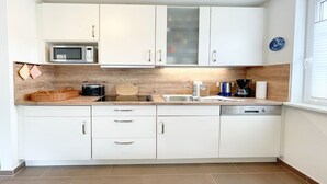 A compact kitchen with white cabinets, a microwave, a coffee maker, and a dishwasher. - Relax in the vacation apartment "Sünnhuus" at the coastal forest in Koserow - Am (Koserow)