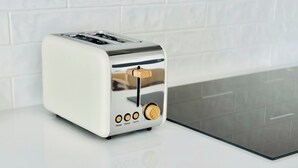 Un tostador blanco con cubierta de acero inoxidable sobre una encimera blanca.