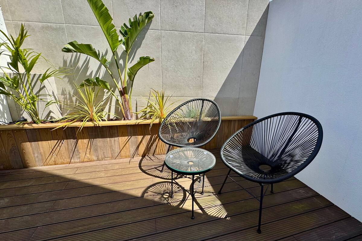 Una terraza de madera con dos sillas de alambre negro y una pequeña mesa de vidrio.