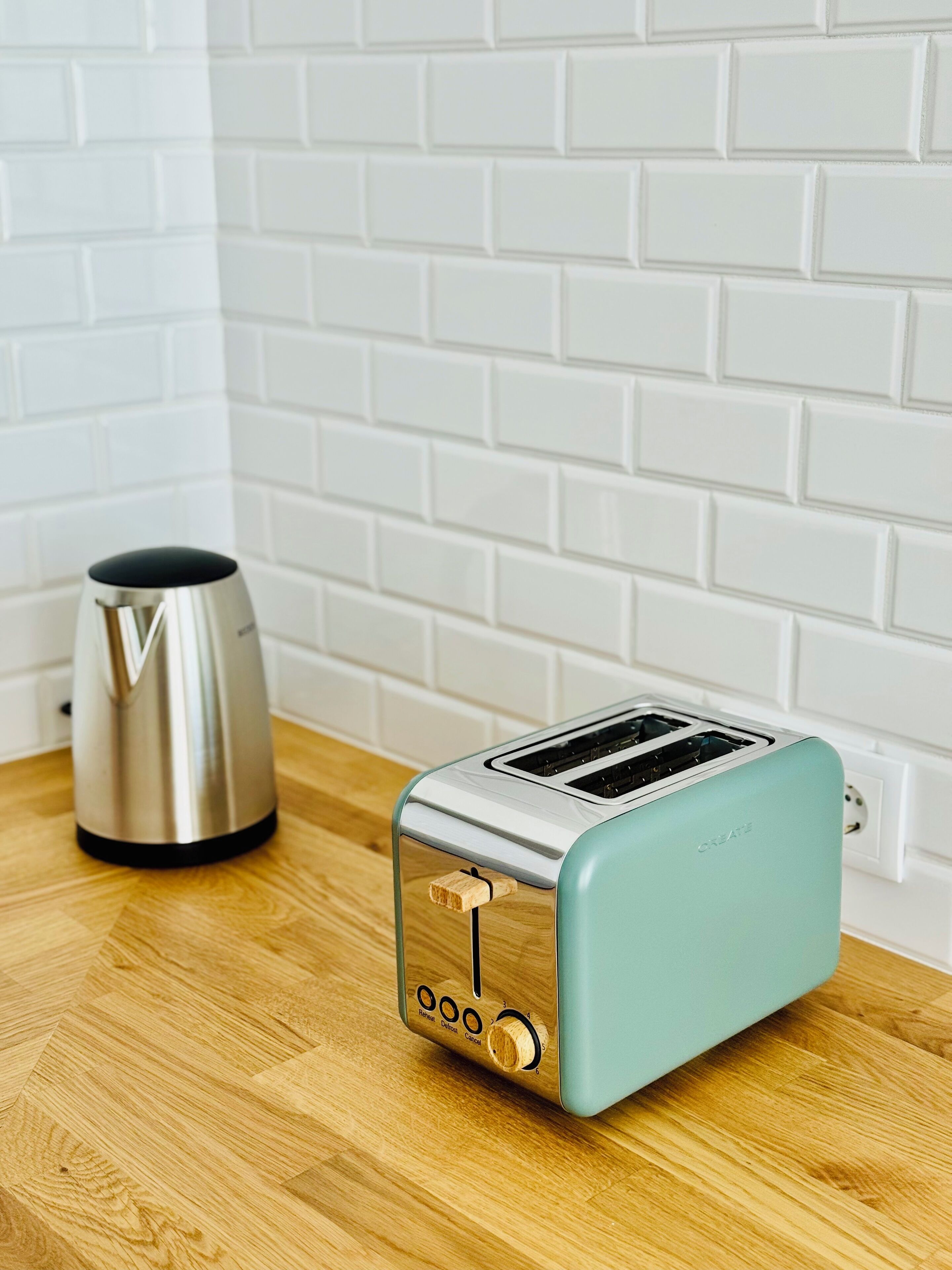 A kitchen with a toaster on a wooden countertop, a kettle, and a white brick wall.